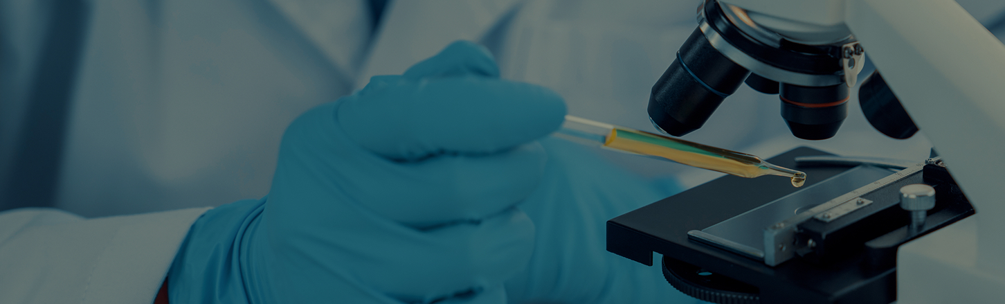 Scientist with an oil dropper putting a drop of amber liquid onto a microscope slide